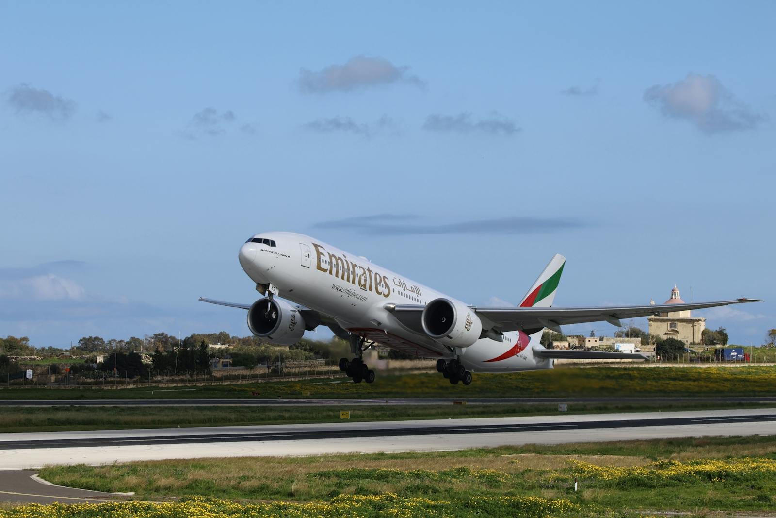 Un aereo Emirates decolla contro un cielo azzurro limpido, perfetto per temi di viaggio.